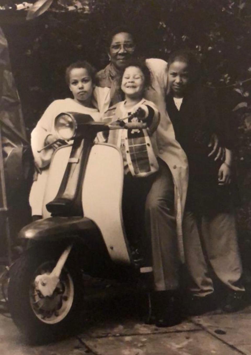 Cynthia smiling with children around a vintage scooter.